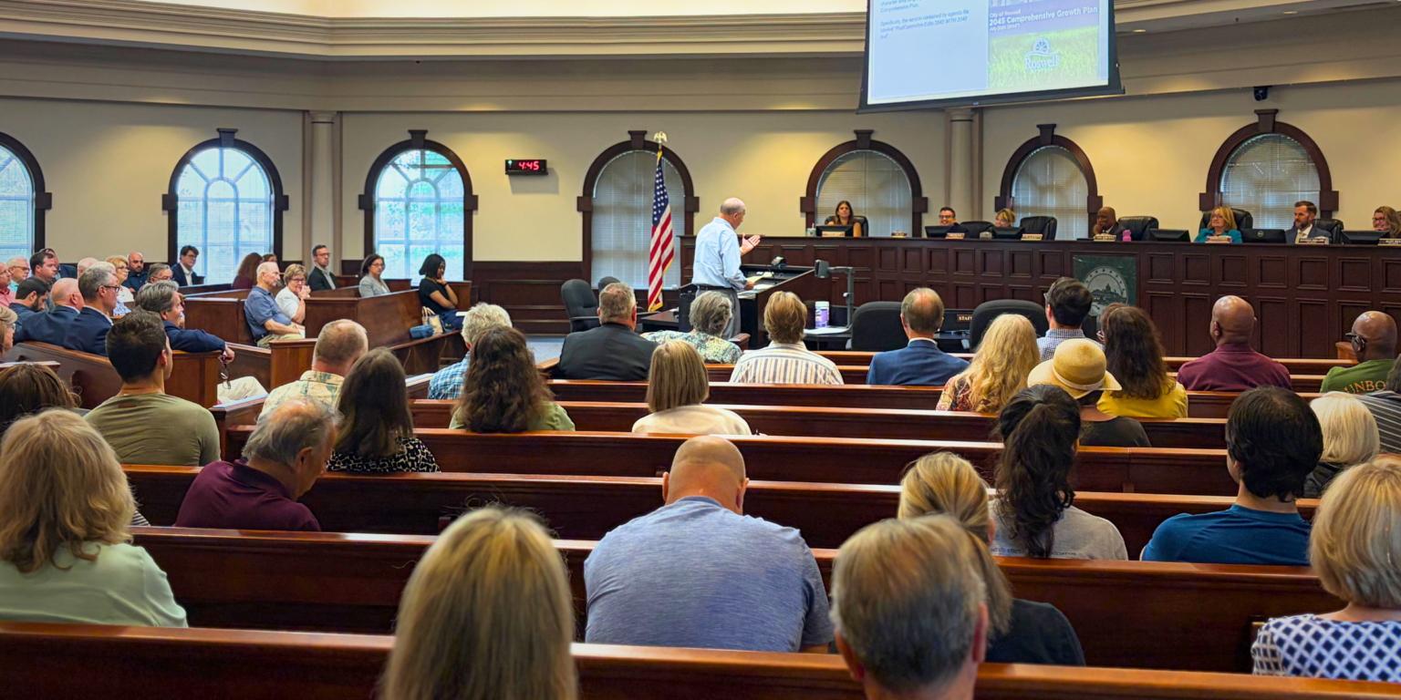 Members of the public sit in pews during a meeting at Roswell City Hall in Council Chambers.