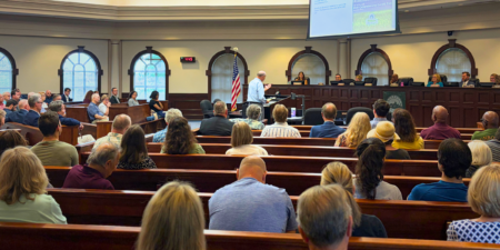 Members of the public sit in pews during a meeting at Roswell City Hall in Council Chambers.